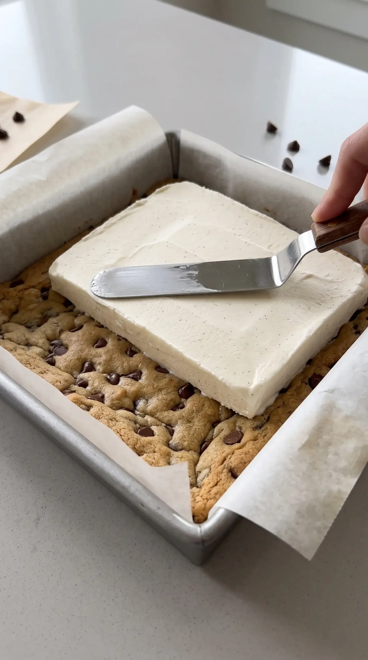 Vanilla ice cream layer being added between cookie layers in a square baking pan