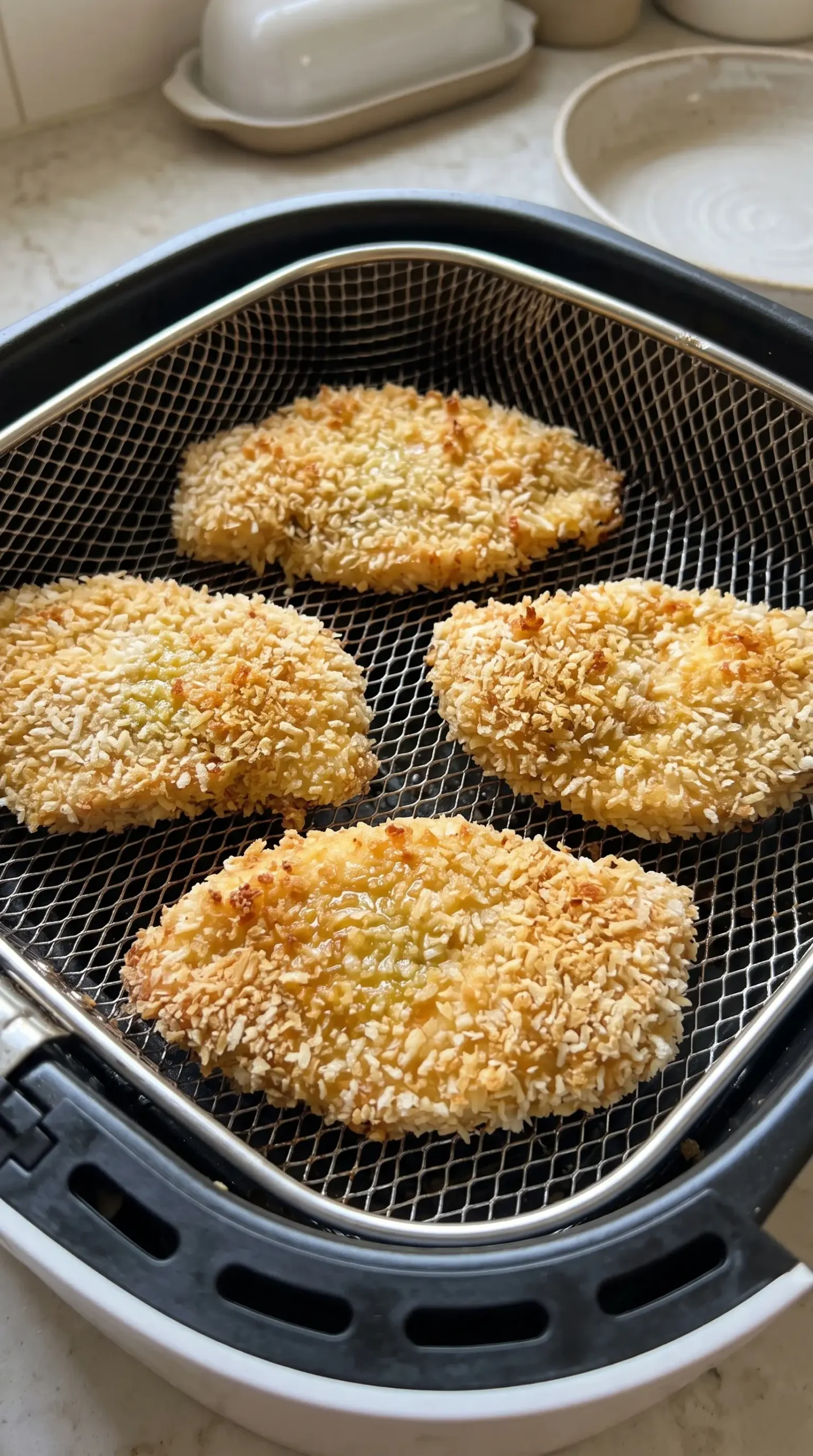 Panko-coated chicken cutlets arranged in an air fryer basket before cooking