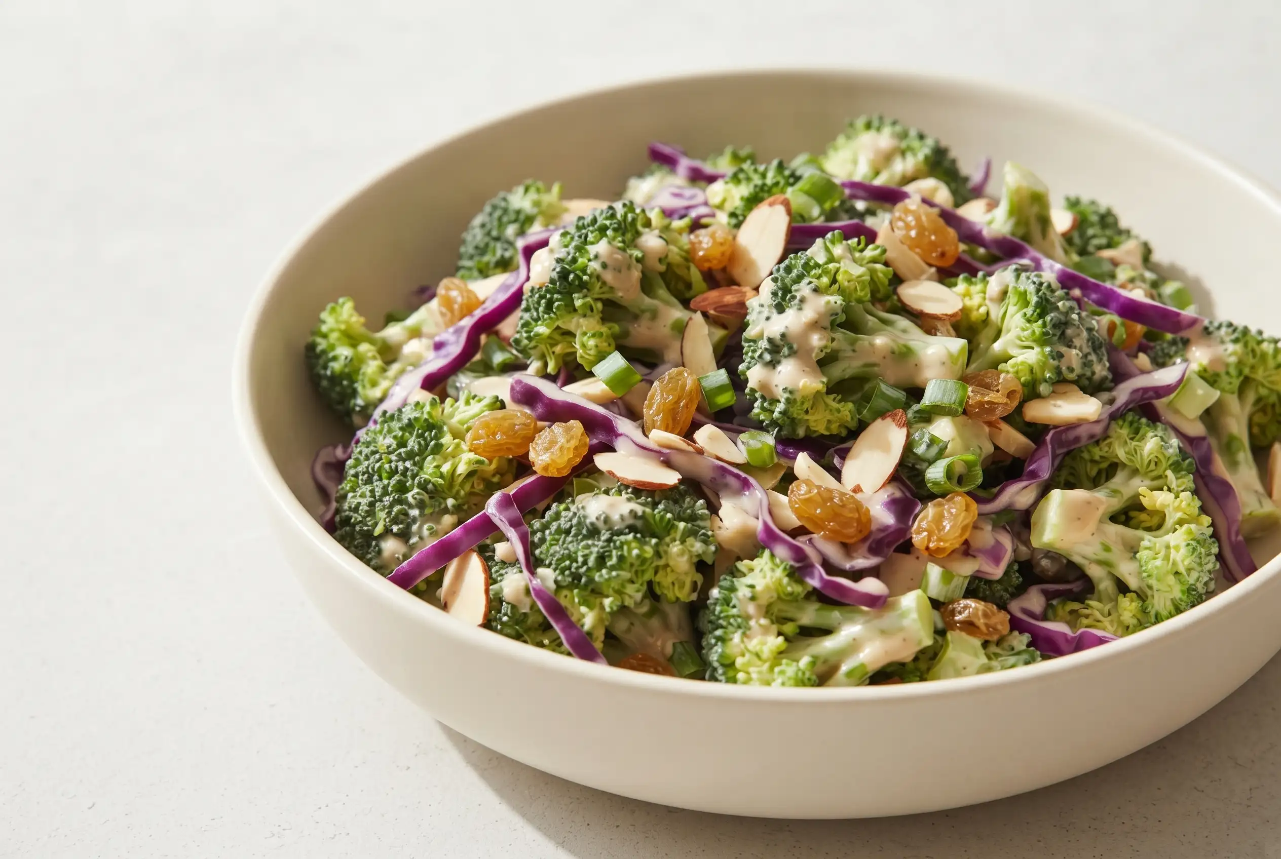 Broccoli salad with creamy almond dressing, purple cabbage, raisins, almonds, and green onions in a bowl