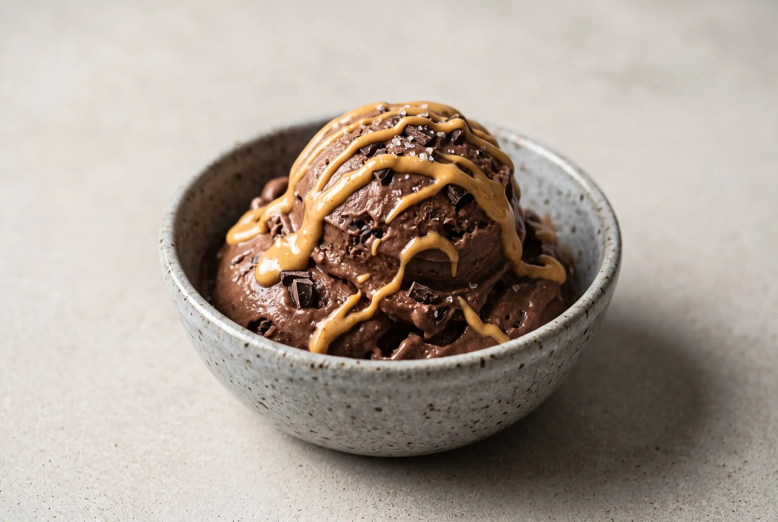 Chocolate Banana Ice Cream with Peanut Butter Chocolate banana ice cream in a bowl with peanut butter drizzle, chocolate pieces, and sea salt