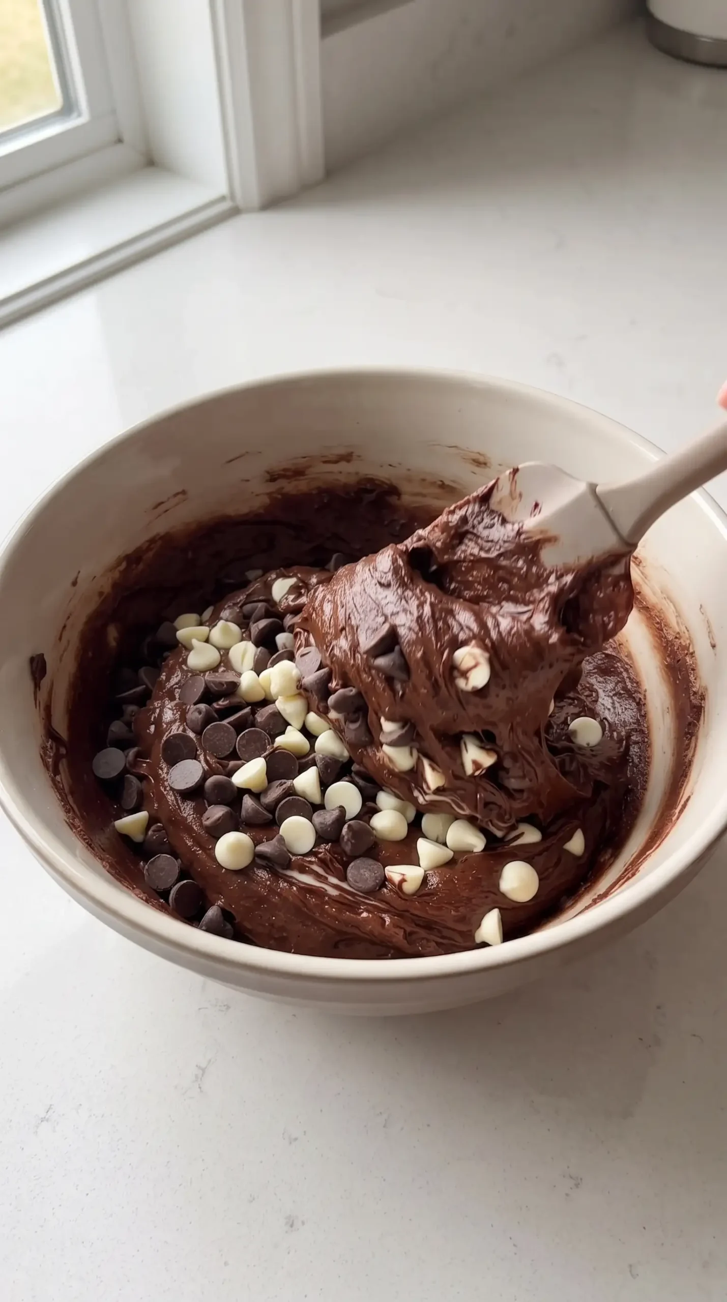 Chocolate cookie dough with dark and white chocolate chips being folded in a bowl