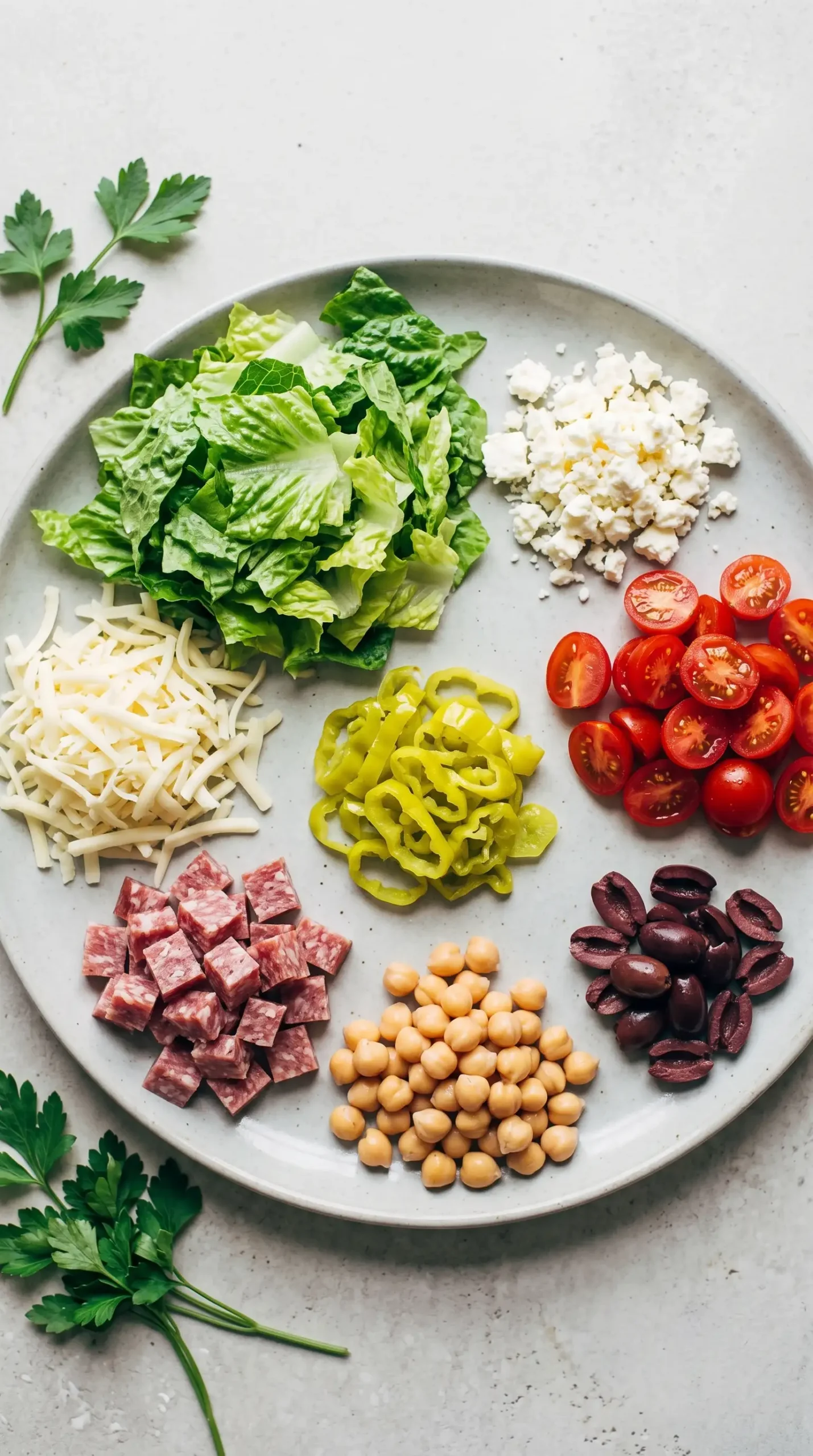 Ingredients for chopped salad pizza including romaine, feta, salami, tomatoes, and pepperoncini
