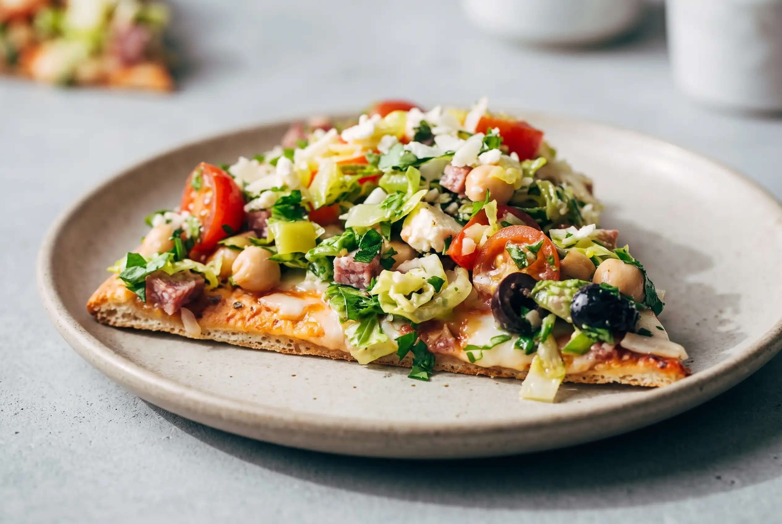 Slice of chopped salad pizza with romaine, feta, salami, pepperoncini, tomatoes, and olives