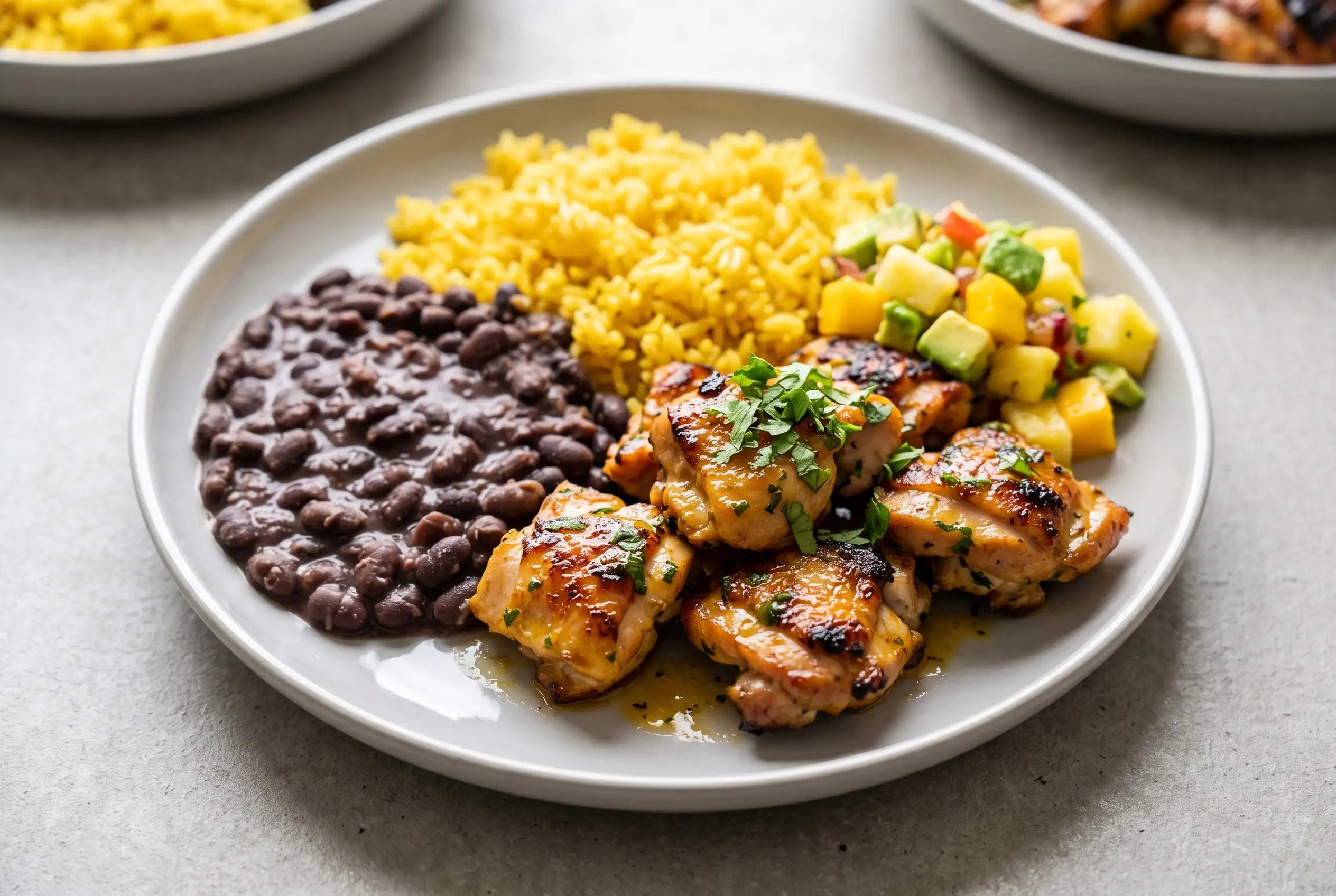 Cilantro orange chicken with yellow rice, black beans, and fruit salsa on a plate