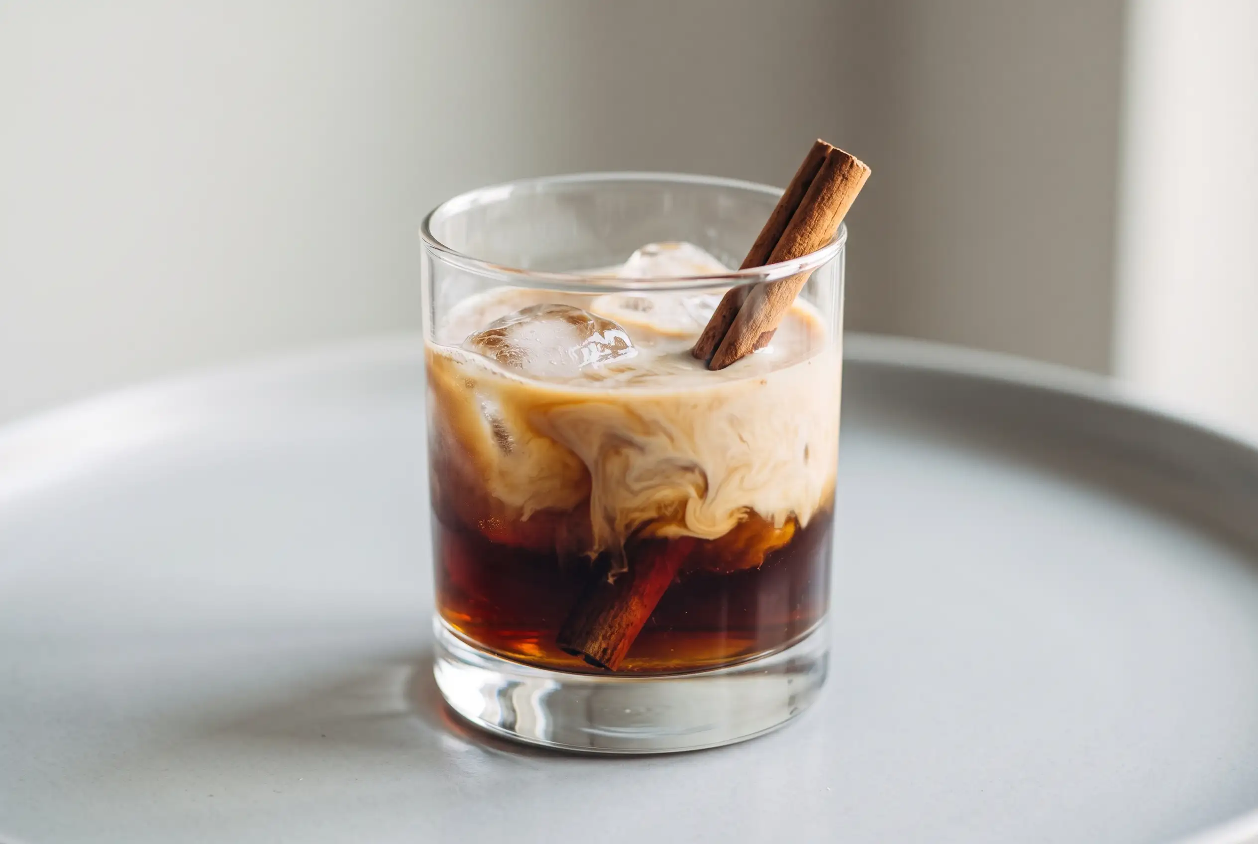 Cinnamon White Russian cocktail with creamy layers, coffee liqueur, ice, and cinnamon stick