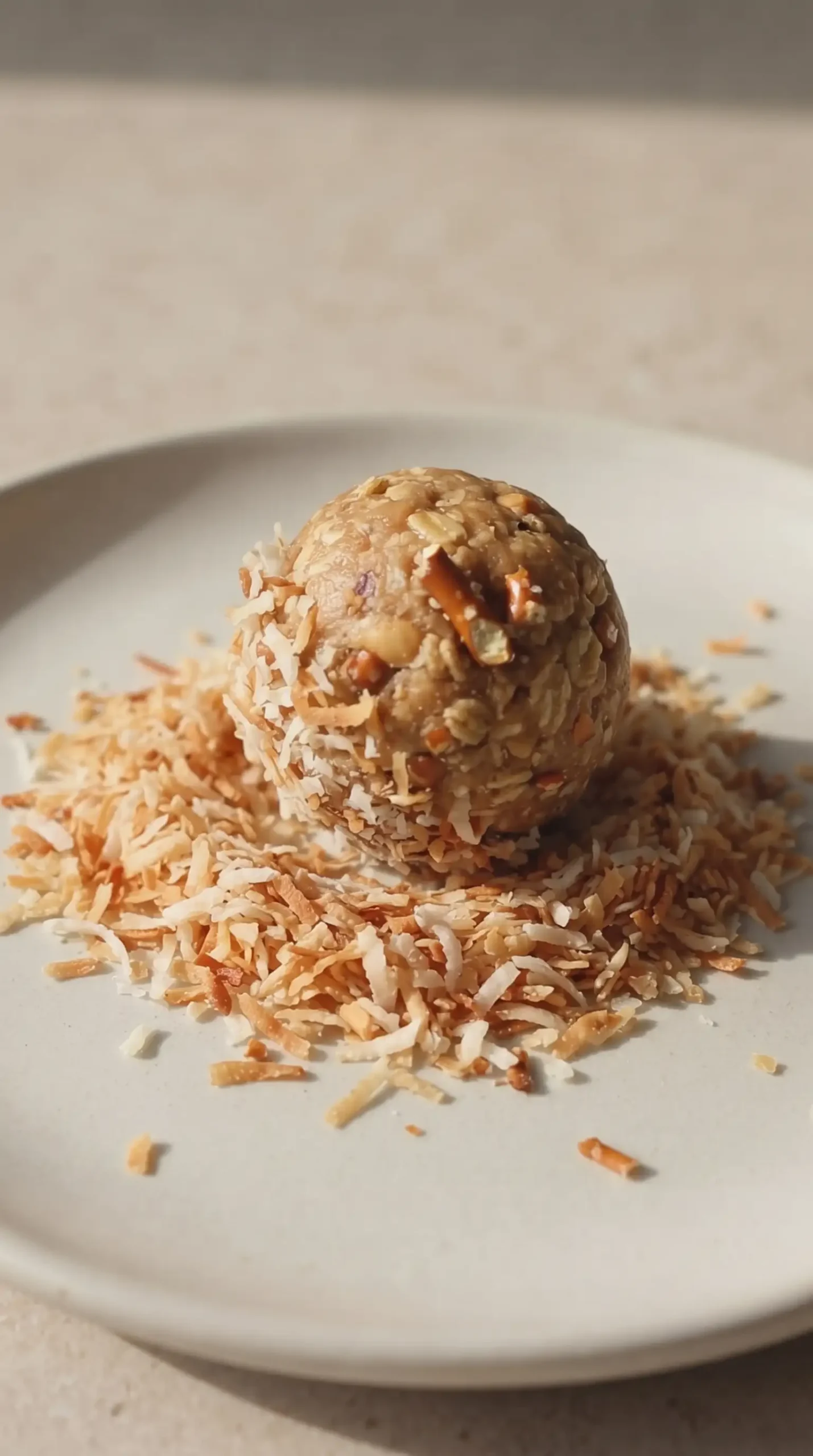Peanut butter pretzel energy bite being coated with toasted coconut flakes