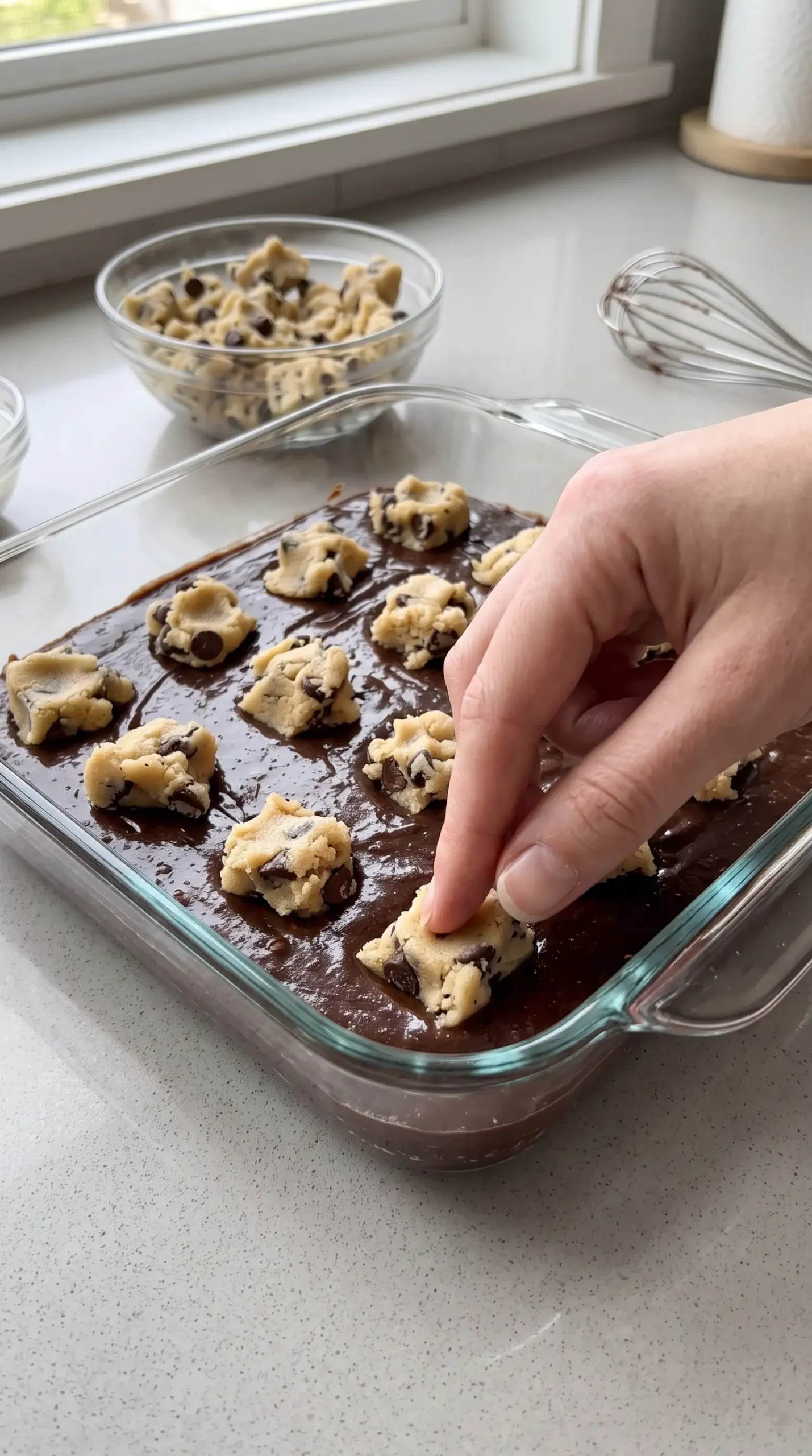 Homemade cookie dough pieces arranged over brownie batter in a baking dish