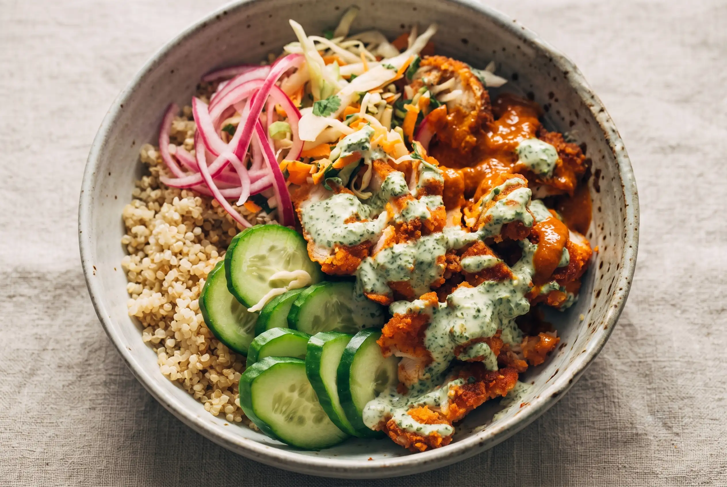 Crispy chicken tikka bowls with quinoa, cucumber, slaw, pickled onions, and mint sauce