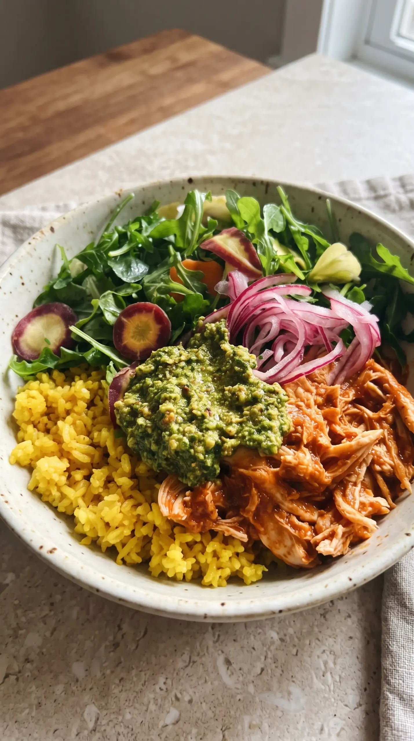 Finished crockpot chicken bowl with yellow rice, shredded chicken, cilantro pesto, greens, and onions