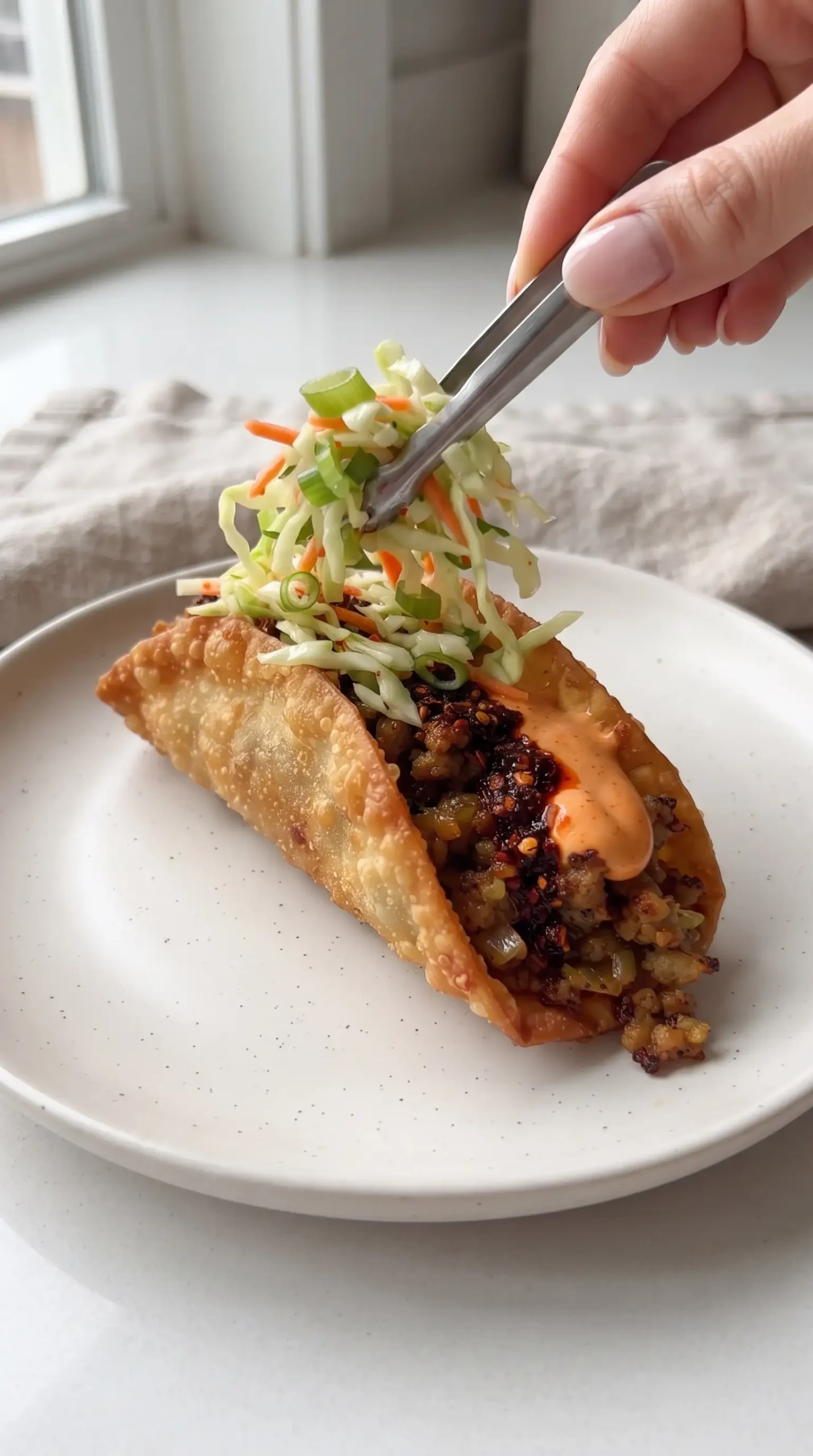 Finished egg roll taco topped with cabbage slaw, green onions, and spicy sauce