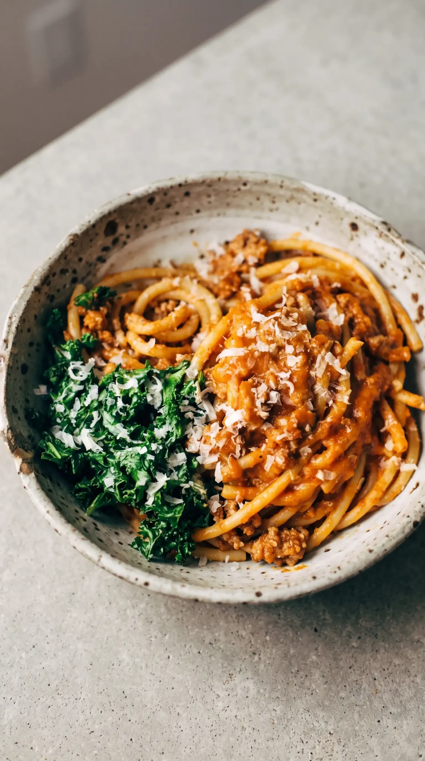 Bowl of pumpkin spaghetti with turkey, garlic kale, sauce, and Parmesan cheese