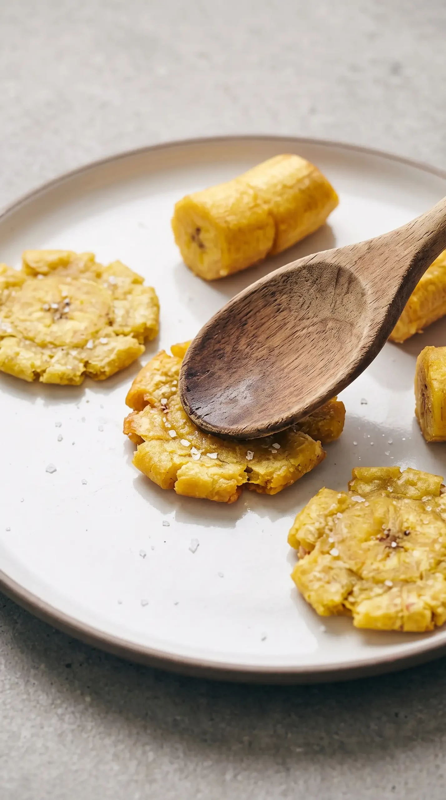 Partially fried plantain pieces being flattened to create tostones edges