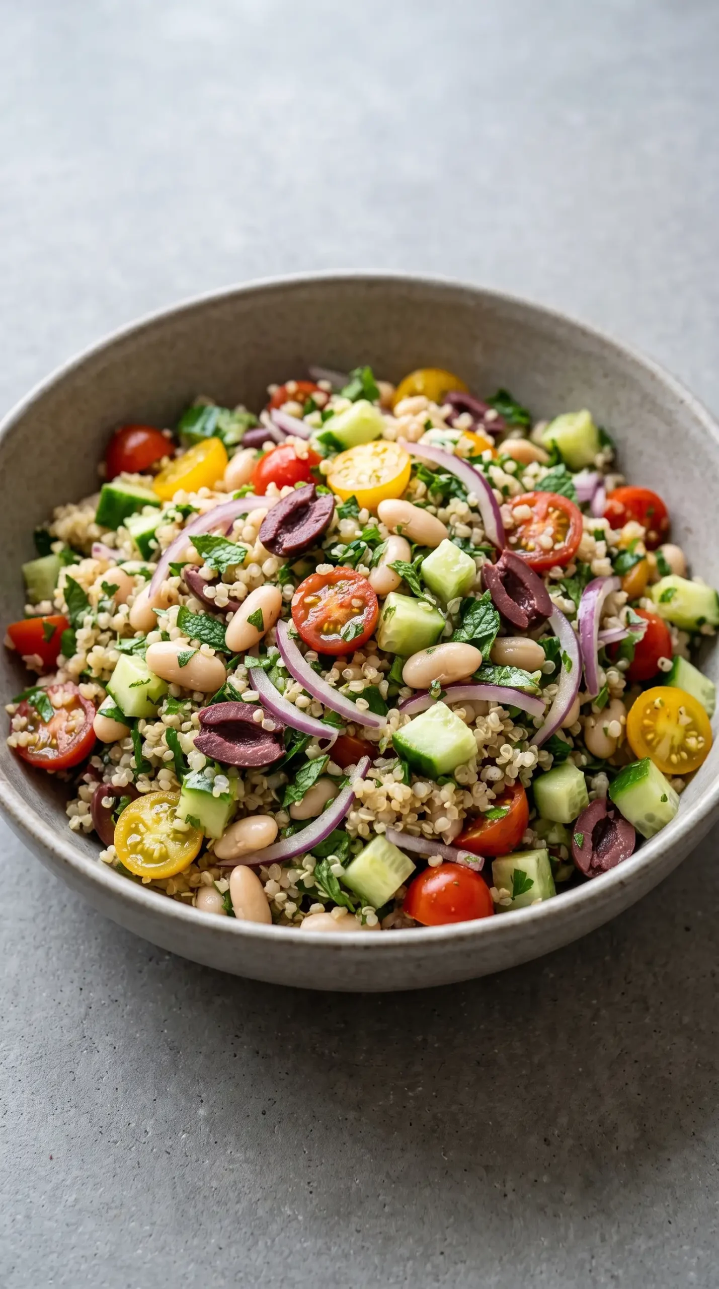 Bowl of Greek salad with quinoa, white beans, chopped vegetables, olives, and herbs
