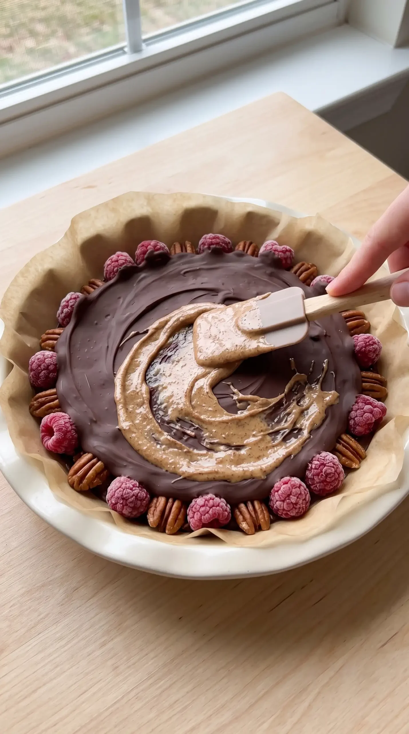 Layered chocolate mixture covering raspberries and pecans in a parchment-lined pie plate