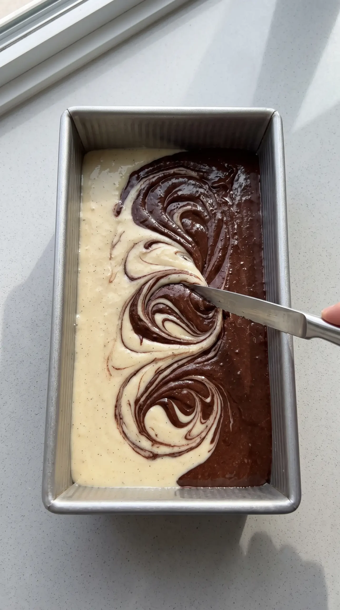Vanilla and cocoa batter layered in a loaf pan before creating the marble swirl