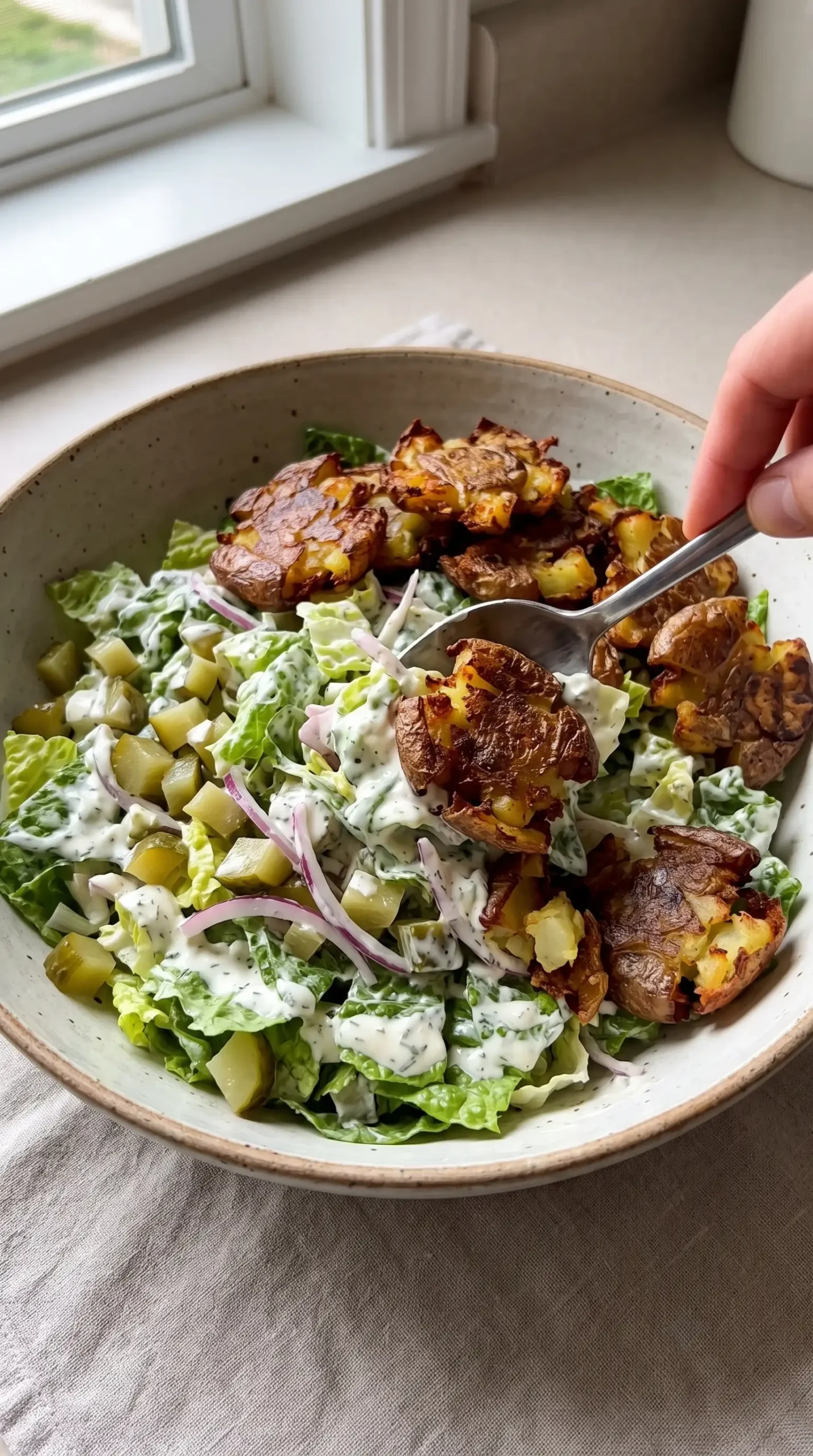 Creamy salad mixture being combined with crispy smashed potatoes