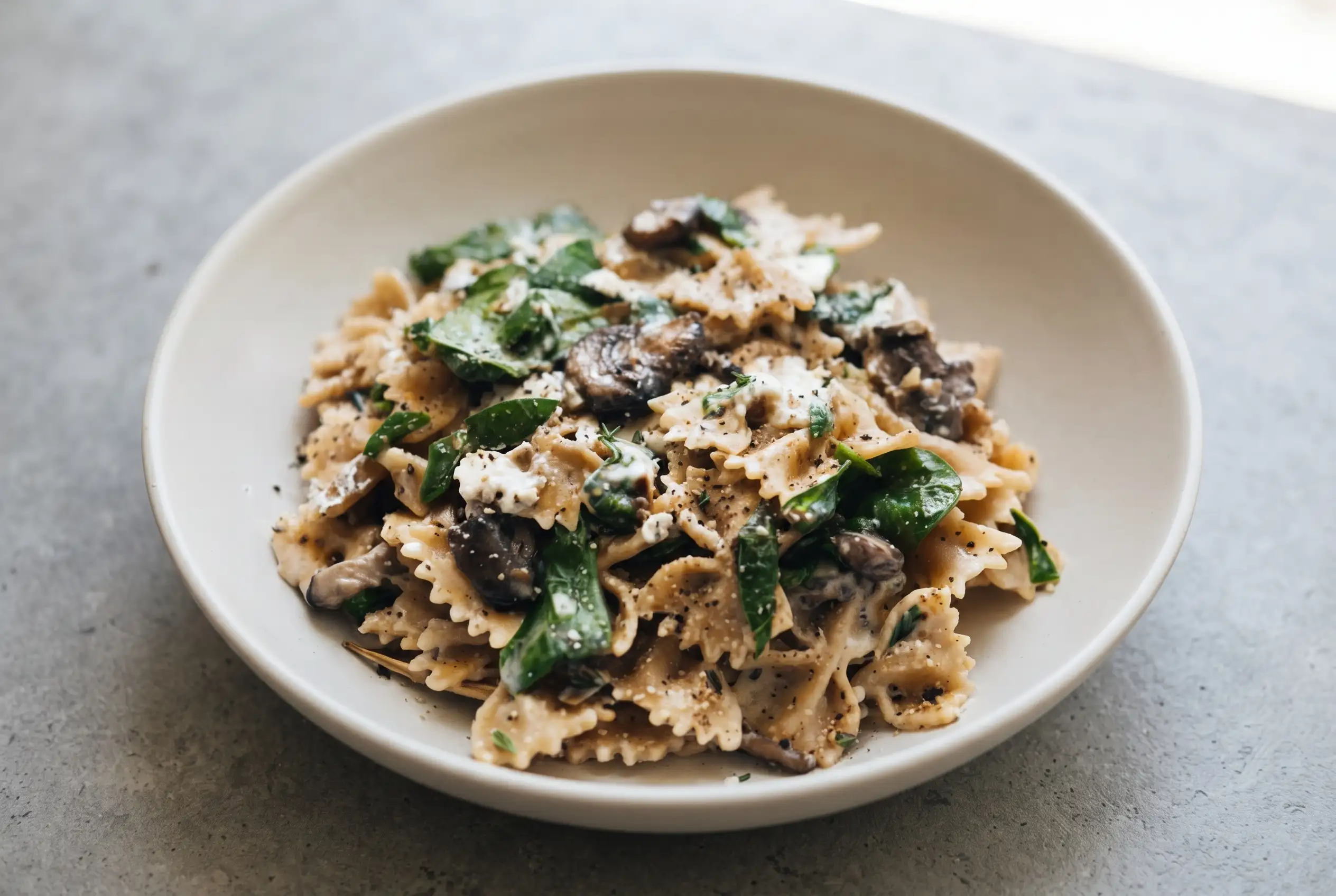 Mushroom goat cheese pasta with creamy sauce, spinach, farfalle, and sautéed mushrooms in a bowl
