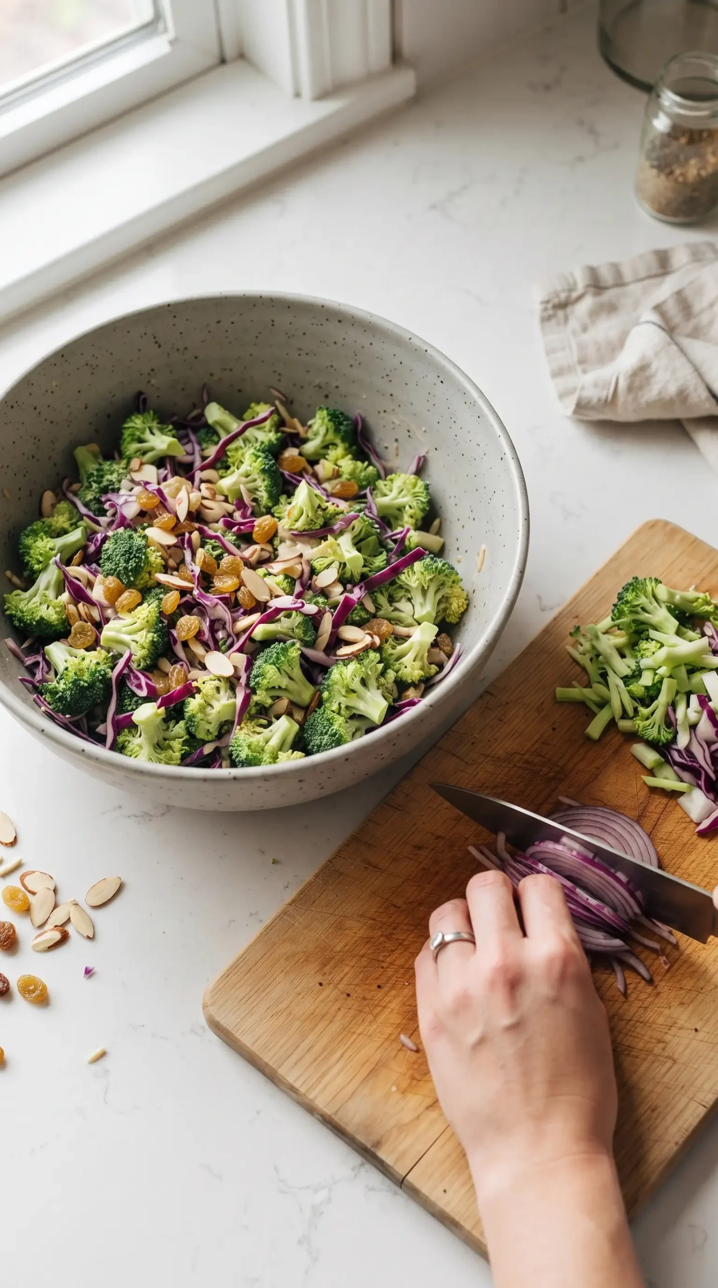 Preparing broccoli salad with chopped florets, cabbage, raisins, almonds, and green onions in a bowl