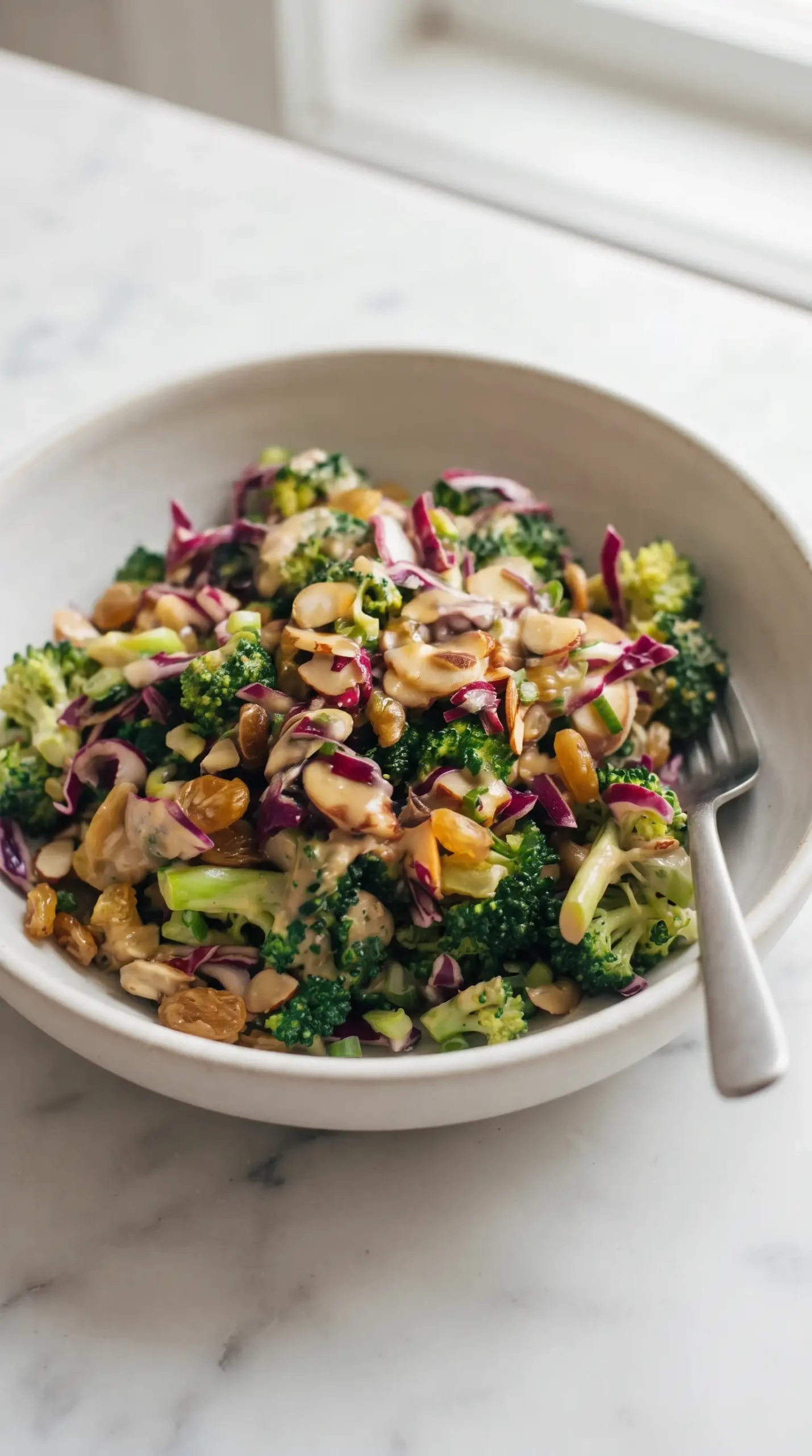 Serving bowl of broccoli salad with creamy almond dressing, raisins, cabbage, and almonds