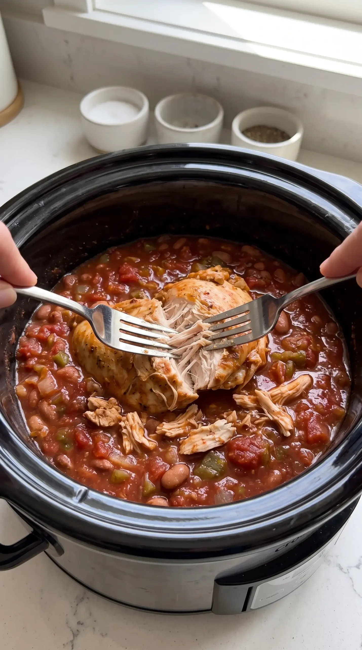 Shredded chicken being prepared with salsa and pinto beans in a slow cooker