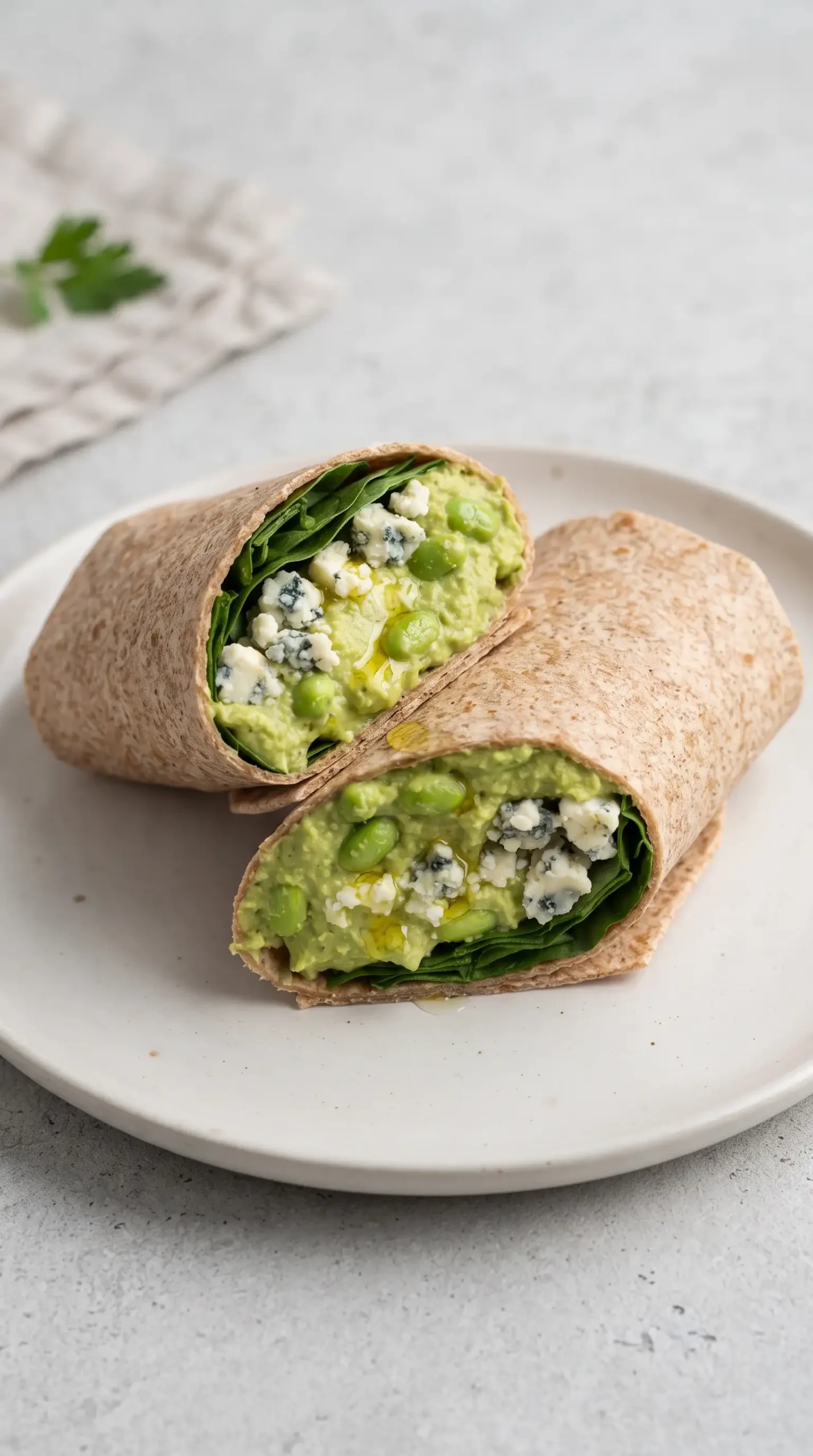 Sliced edamame hummus wrap showing green hummus, spinach, blue cheese, and olive oil