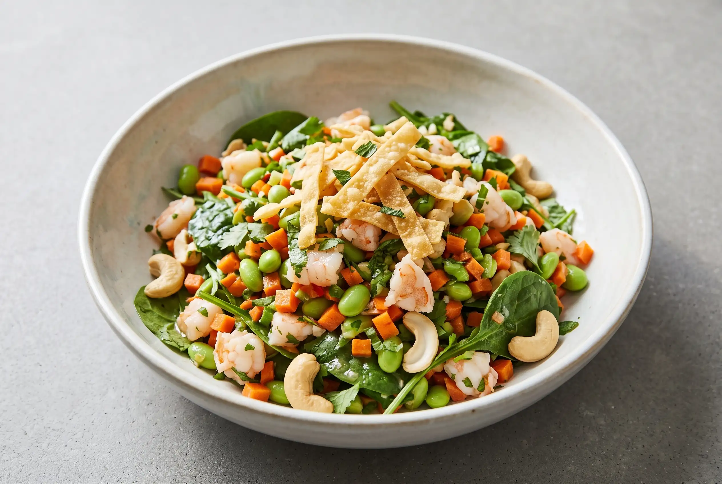 Thai shrimp salad with garlic lime dressing, vegetables, herbs, cashews, and crispy wonton strips in a bowl