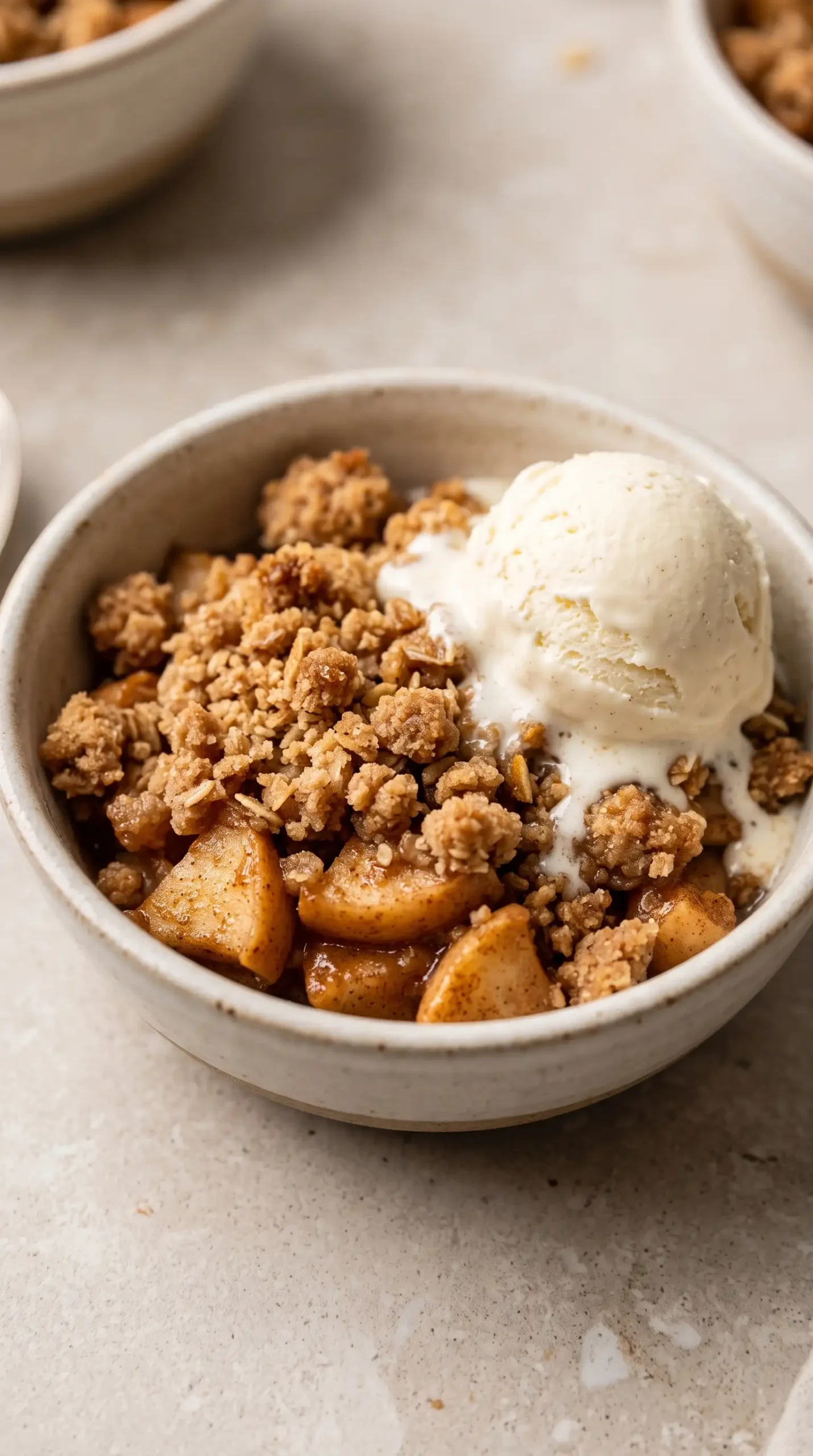 Warm apple crisp serving with brown sugar oat topping and melting vanilla ice cream